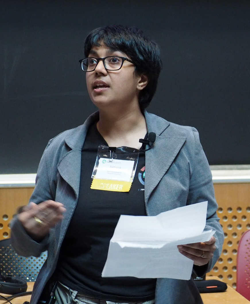 [ A photo of Sumana Harihareswara. She is standing in front of a black board, delivering a talk. She is wearing a black shirt and a grey blazer. ]