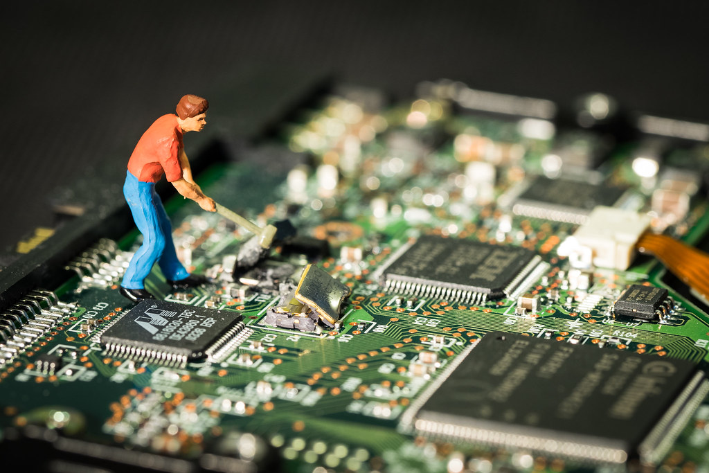 A small clay person with a sledgehammer destroying a large motherboard.