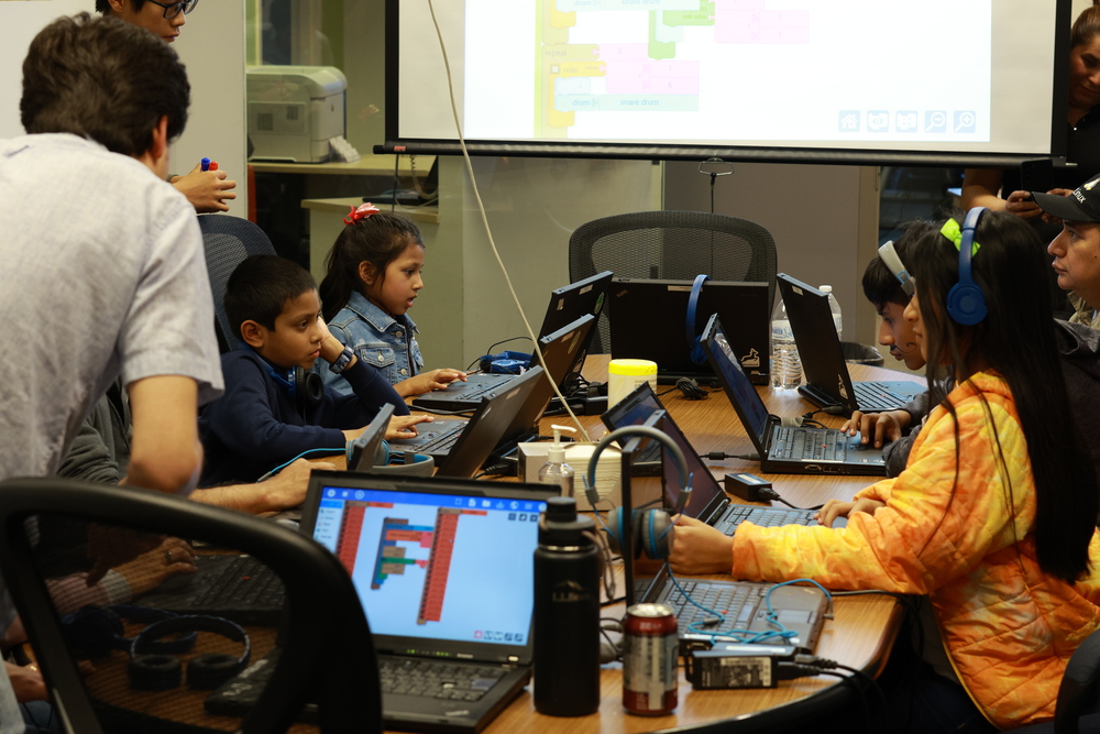 Families gathered around X200s with headphones and colorful displays of visual code.