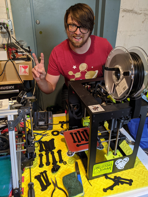 FSF Web Developer Michael McMahon poses with the 3D printers in his garage that are being used to manufacture protective gear and medical supplies in the HACKERS and HOSPITALS initiative..